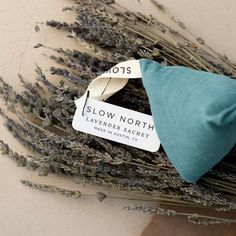 lavender flowers and a blue pillow on a white tablecloth with the label slow north lavender & sachets