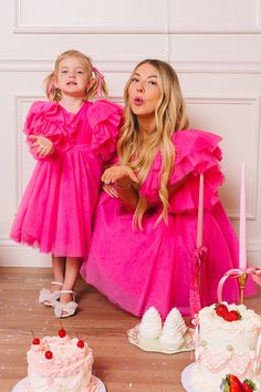 two girls in pink dresses standing next to cake