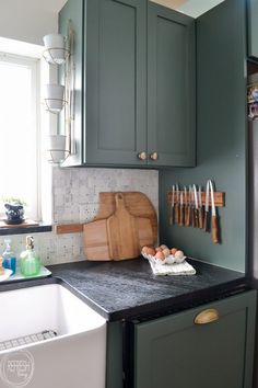 a kitchen with green cabinets and cutting board on the counter top, next to a sink