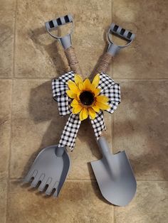 two gardening utensils and a sunflower on a tile floor with black and white checkered ribbon