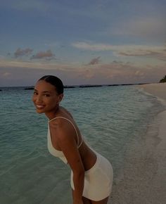 a woman standing on top of a sandy beach next to the ocean in front of an island