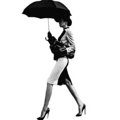 a black and white photo of a woman walking with an umbrella over her head while wearing high heels