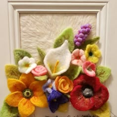 an arrangement of felt flowers is displayed in front of a white frame