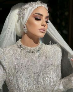 a woman in a white dress with veil and diamond jewelry on her head is looking at the camera