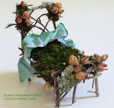 a miniature chair made out of branches with flowers and moss on the seat is covered in blue fabric