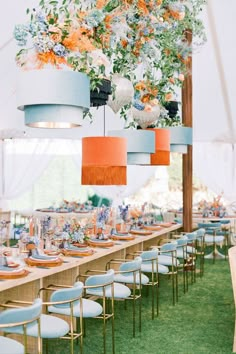 a long table with blue chairs and orange lamps hanging from it's centerpieces