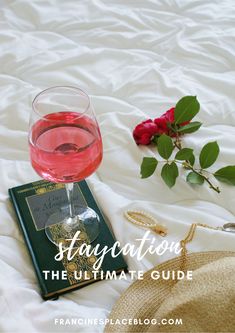 a glass of wine sitting on top of a bed next to a book and rose