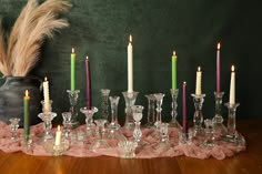 a table topped with lots of glasses and candles next to a vase filled with feathers