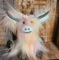 a stuffed animal with long hair and flowers on it's head sitting in a wooden box