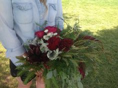 a woman holding a bouquet of flowers in her hands on the grass near some trees