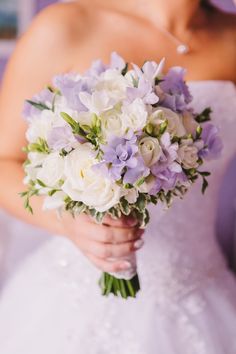 a bride holding a bouquet of white and purple flowers