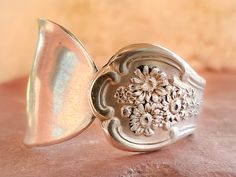 a silver ring with flowers on it sitting on top of a pink cloth covered surface