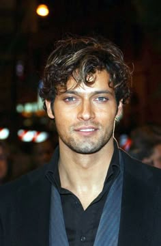 a close up of a person wearing a black shirt and blazer with ear rings