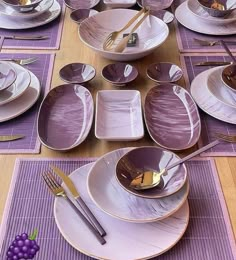 the table is set with purple and white dishes, silverware, and gold cutlery