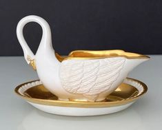 a white swan shaped tea cup and saucer on a gold rimmed dish,