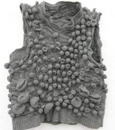 a gray sweater with lots of balls on the front and back, sitting on top of a white surface