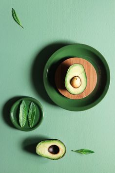 an avocado cut in half sitting on a green plate next to another piece of fruit