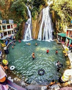 people are swimming in the water near a waterfall