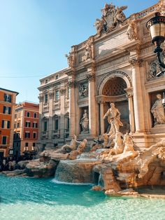 a fountain in front of a building with statues on the sides and water running down it