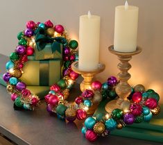 two candles are sitting on a table next to some ornaments and a box with a bow