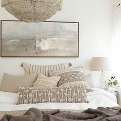 a bed with pillows and blankets on top of it next to a painting hanging above the bed