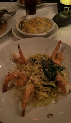 some shrimp and noodles are on a white plate at a table with other dishes in the background