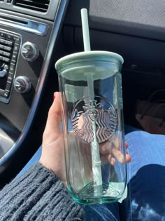 a person holding a starbucks cup in their hand while sitting next to a car steering wheel