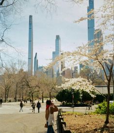 people are walking around in the park with skyscrapers in the backgroung