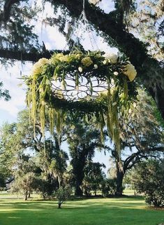 an outdoor wedding venue with lush green grass and hanging flowers on the tree branches in front of it