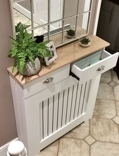 there is a mirror on the wall above a white cabinet with drawers and plants in it