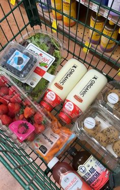 a shopping cart filled with lots of food next to bottles of juice and condiments