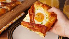 a person holding up a piece of bacon and egg pizza