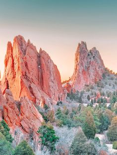 the mountains are covered in red rocks and green trees, as the sun is setting