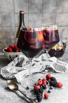 two wine glasses filled with raspberries and blackberries on top of a table