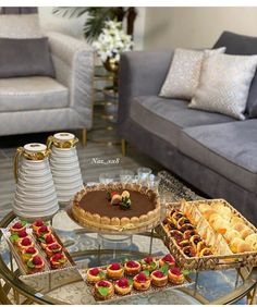 a table topped with cakes and pastries on top of a glass table next to couches