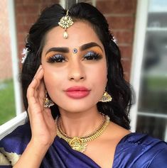 a woman in a blue sari with gold jewelry on her neck and hands near her face