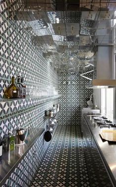 a kitchen with black and white tiles on the walls, counters and shelves filled with pots and pans