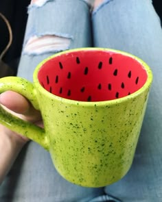 a person holding a green and red coffee cup with black spots on it's side