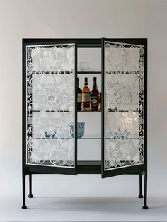 an open cabinet with bottles and glasses on the top, in front of a white wall