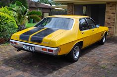 a yellow and black car parked in front of a brick house next to a tree