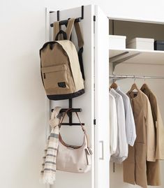 an open closet with clothes and handbags hanging on the door handle, in front of a white wall