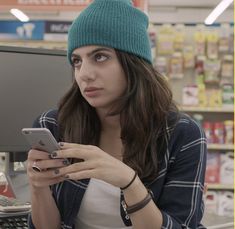 a woman in a store looking at her cell phone while she's on the computer