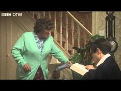 an older woman standing next to a young man in front of a stair case holding a piece of paper