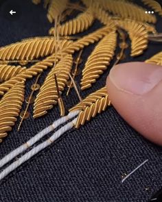 someone is stitching gold leaves on a piece of fabric