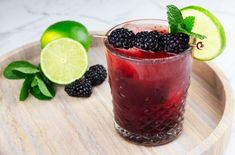 two glasses filled with blackberries and limeade on top of a wooden cutting board