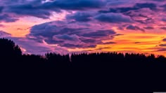 the sun is setting over a field with trees in the foreground and clouds in the background