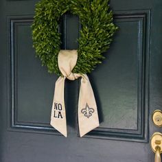 a green door with a wreath and nola on it's side hanging from the front door