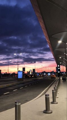 an empty parking lot at night with the sun setting in the distance and clouds above