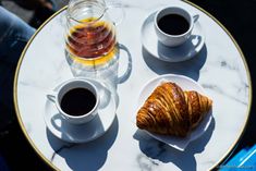 two croissants are sitting on a table with cups of coffee and tea