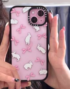 a woman holding up a pink phone case with white rabbits on it